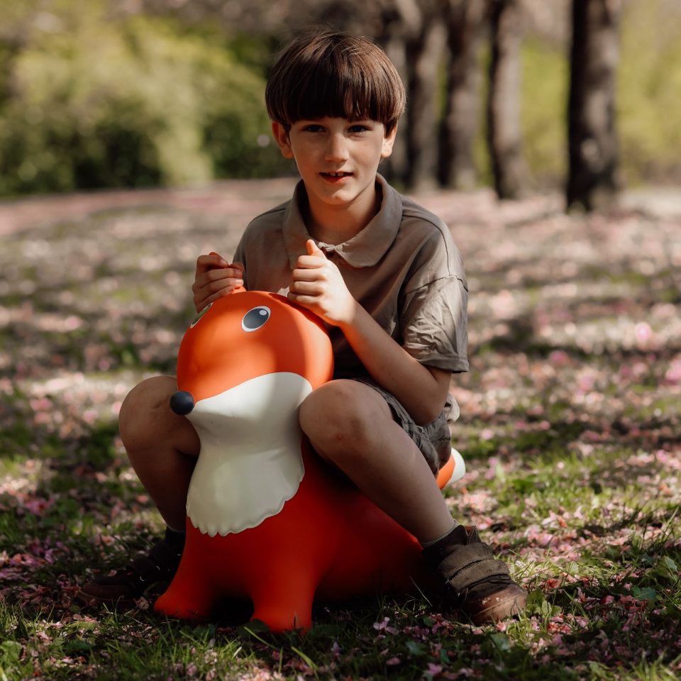 Kind sitzt auf dem orangefarbenen Springer Fuchs von Find that Hippo im Freien