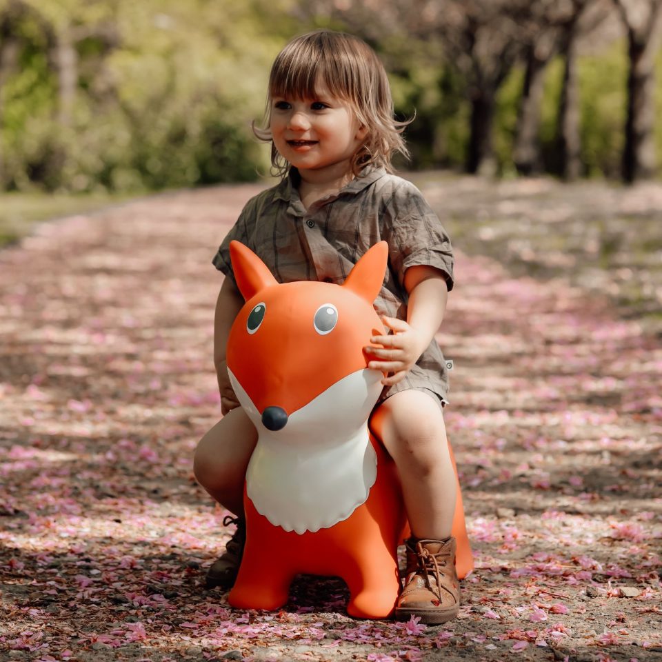 Kind sitzt auf dem orangefarbenen Springer Fuchs von Find that Hippo im Freien