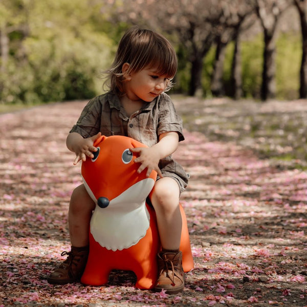 Kind sitzt draußen auf dem orangen Springer Fuchs von Find that Hippo auf einem gepflasterten Weg