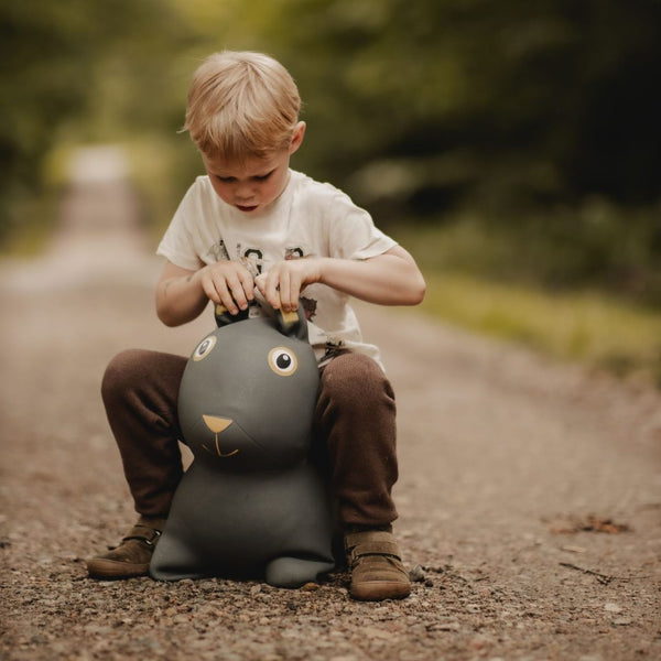 Kind sitzt auf einem grauen Springer Hase Skoczek von Find that Hippo auf einem Waldweg