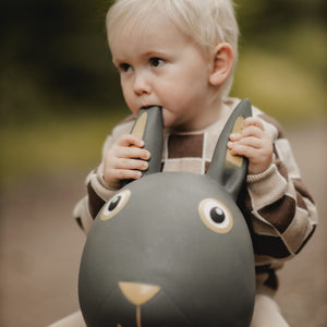 Kleines Kind sitzt auf grauem Springer Hase Spielzeug von Find that Hippo im Freien